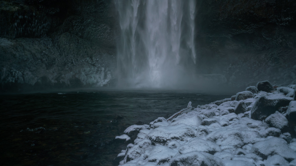 A tall waterfall pouring into a snow-ringed canyon