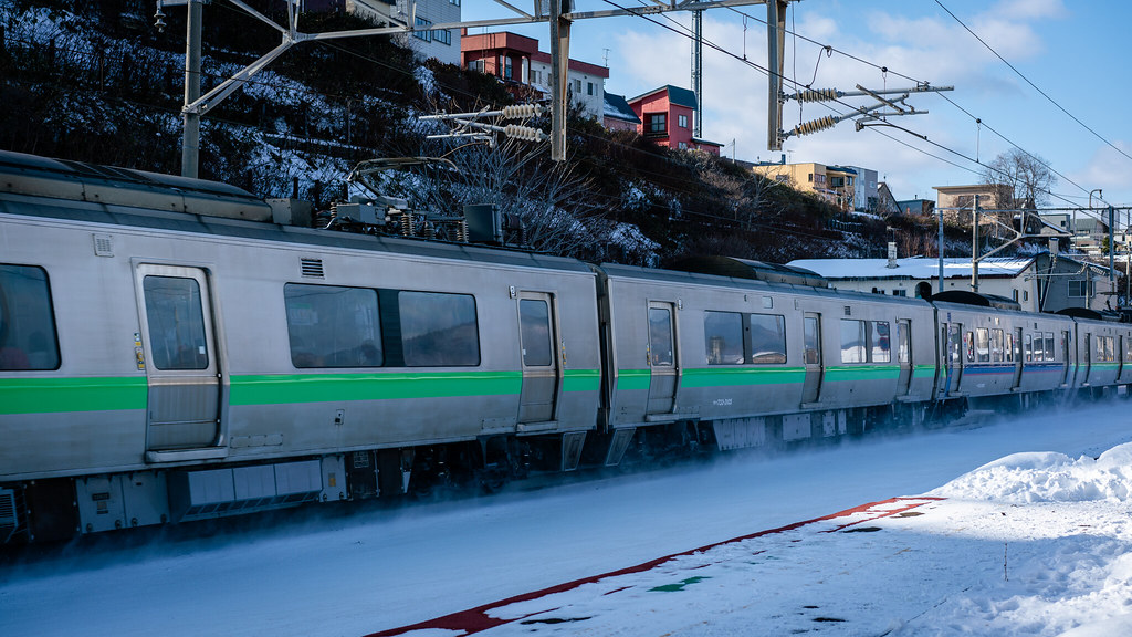 A green commuter train running along snowy tracks