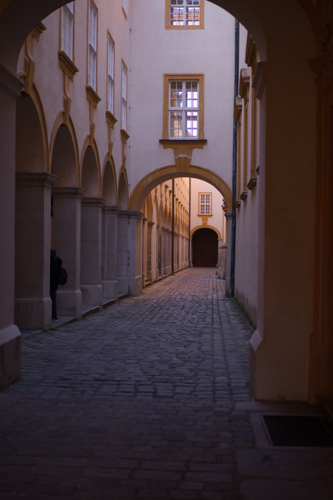 A lone figure in a warm-lit arched passage at Melk Abbey