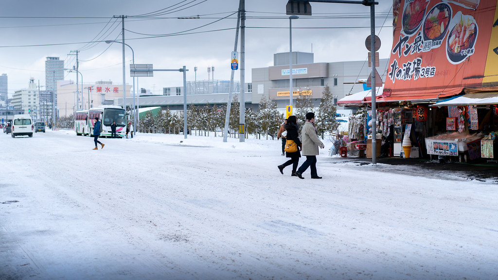 A snow-covered street with shoppers passing a fish market storefront