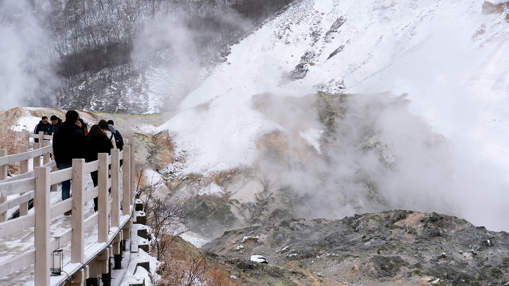 Steam rising from a volcanic valley with a boardwalk of visitors